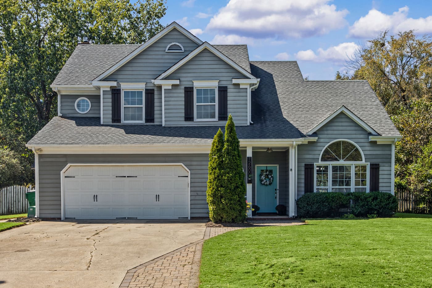 The front of 12600 Parks Farm Lane: a gray two-story home with black shutters, an attached two-car garage, a turquoise front door and a green front lawn.
