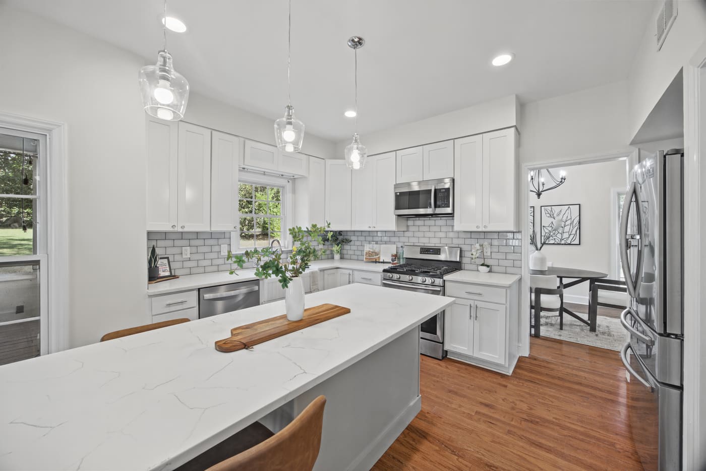 The kitchen with white shaker cabinets, a quartz-topped island, glass pendant lights and a gas range under a stainless microwave.