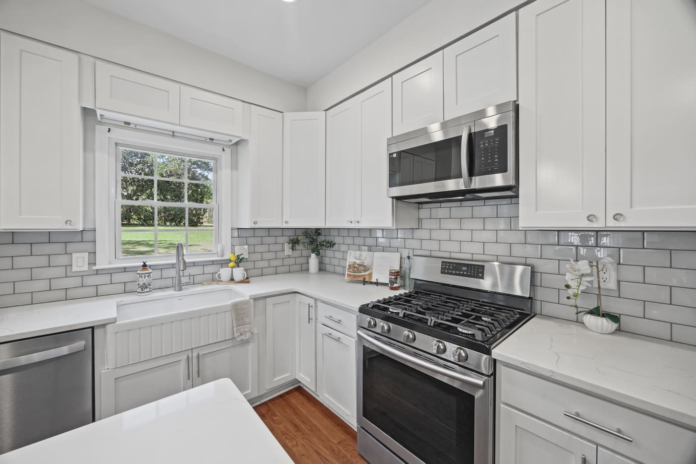 The stainless gas range beneath a new stainless microwave, set in white cabinetry and subway tile.