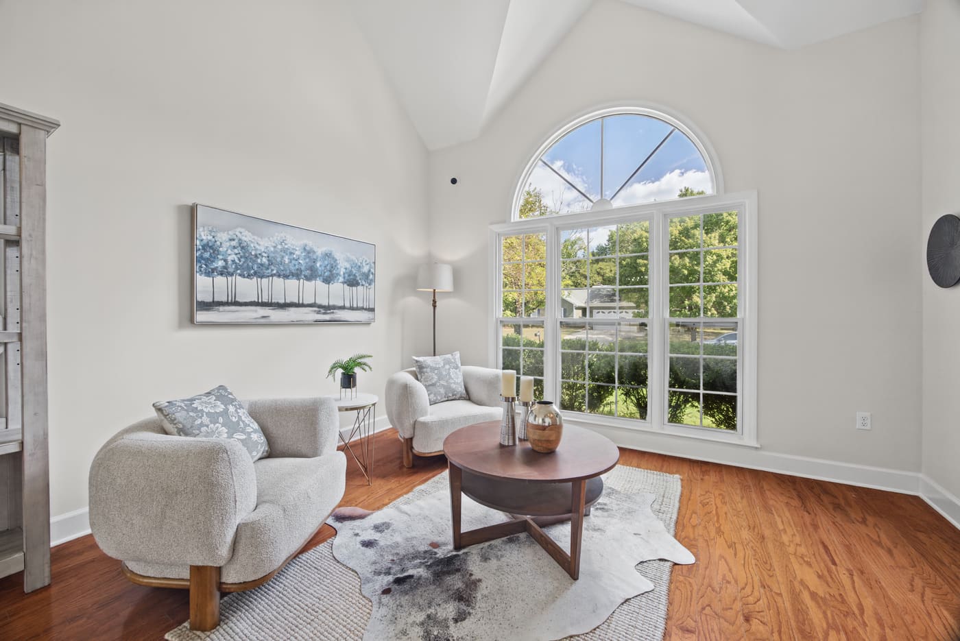 The living room under a vaulted ceiling, lit by a tall arched window over the front lawn.