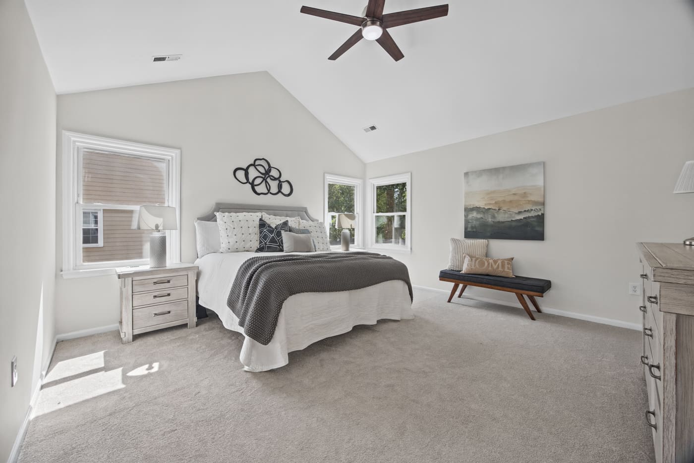 The primary bedroom under a vaulted ceiling, with a ceiling fan and windows on two walls.